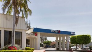 A motel with a covered parking area, palm trees, and a clear sky.
