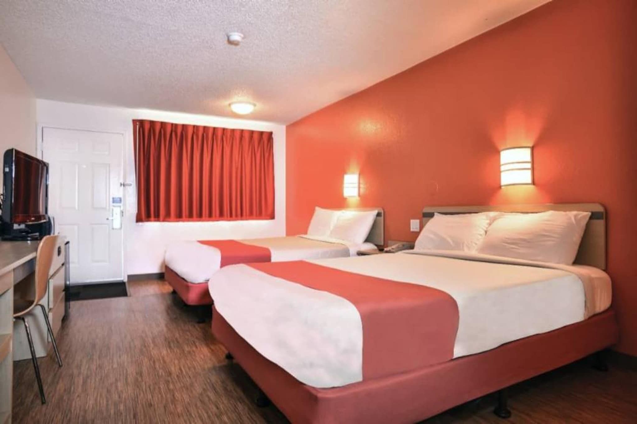 A hotel room with two beds, a desk, and a television.