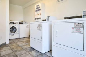 A laundry room with a front-loading washer and dryer, a wall-mounted soap and bleach dispenser, and a sign indicating the room's purpose. - Spacious room, 2 double beds | Accessible/Bathtub (Saint Joseph)