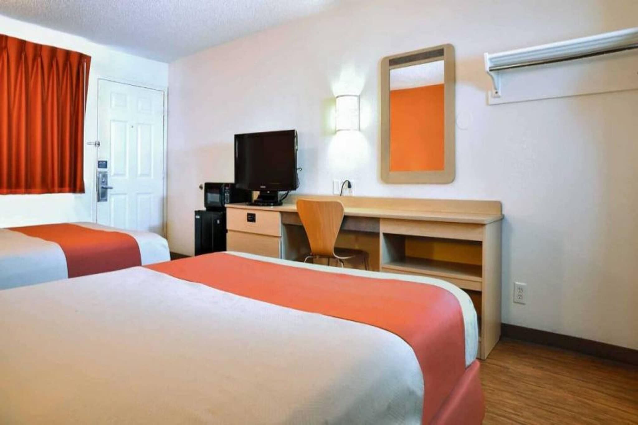 Une chambre d’hôtel avec deux lits, un bureau, une chaise, une télévision et un miroir.