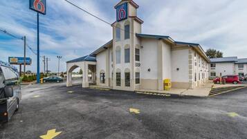 A motel with a prominent '6' sign, a covered parking area, and a clear sky.