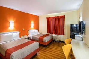 A hotel room with two beds, a desk, a television, and a window with curtains.