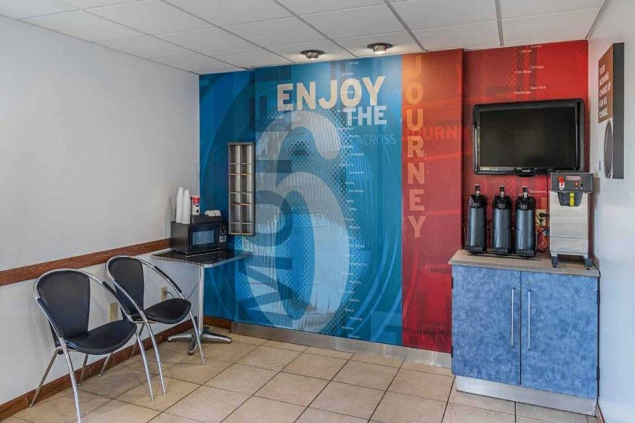 Una habitación con pared azul y roja, un escritorio con computadora, dos sillas, un televisor y un armario con extintores.