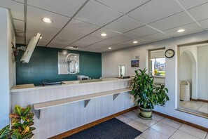 A reception desk with a green accent wall, a clock, and a potted plant.