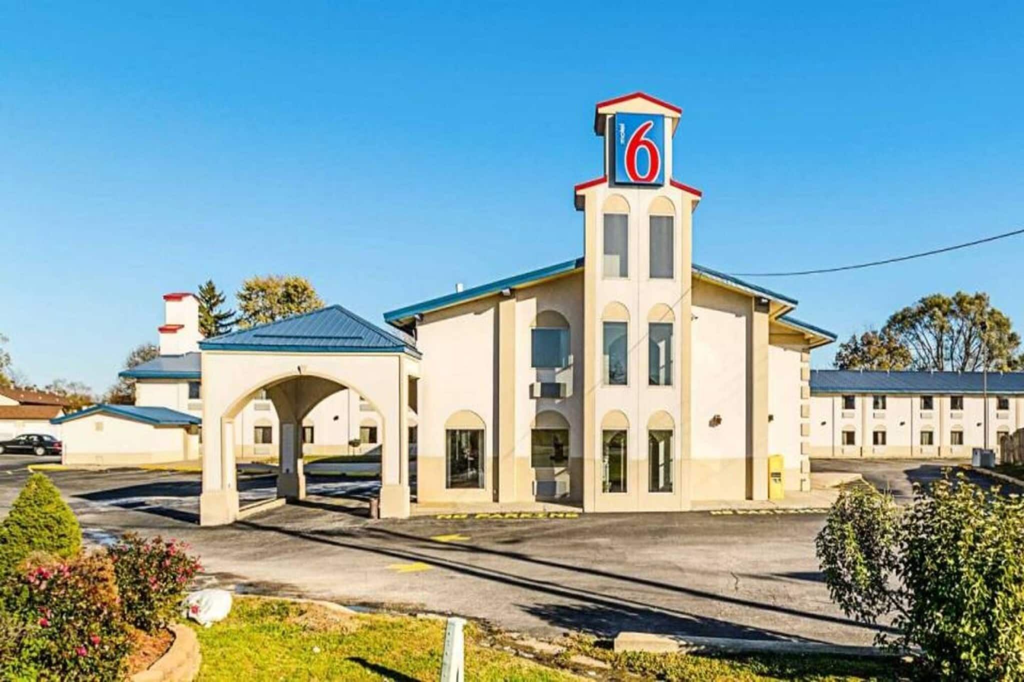 Et motel med et tydeligt skilt med '6', et overdækket parkeringsområde og en klar himmel.