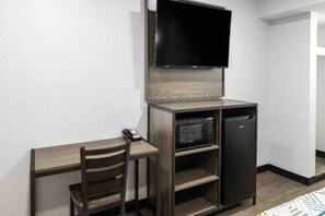 A compact room with a desk, chair, television, and a small refrigerator.
