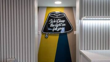 Ein Flur mit einem Neonlichtschild an der Wand, auf dem steht: 'Wir lassen das Licht für Sie an.'