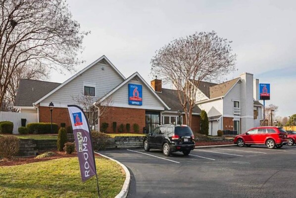 A hotel with a '6' sign, a 'New Rooms' banner, and a parking lot with cars. - 1 Queen Bed | Non-Smoking (Greensboro)