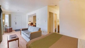 Une chambre d’hôtel avec un lit, un canapé, une petite table et une chaise. Une porte donne accès à la salle de bain.
