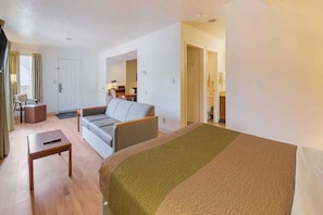 A hotel room with a bed, a sofa, a small table, and a chair. There is a door leading to a bathroom. - 1 Queen Bed | Non-Smoking (Greensboro)