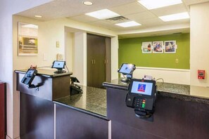 A reception area with two reception desks, a green wall with framed pictures, and a fire alarm on the right. - 1 Queen Bed | Non-Smoking (Greensboro)