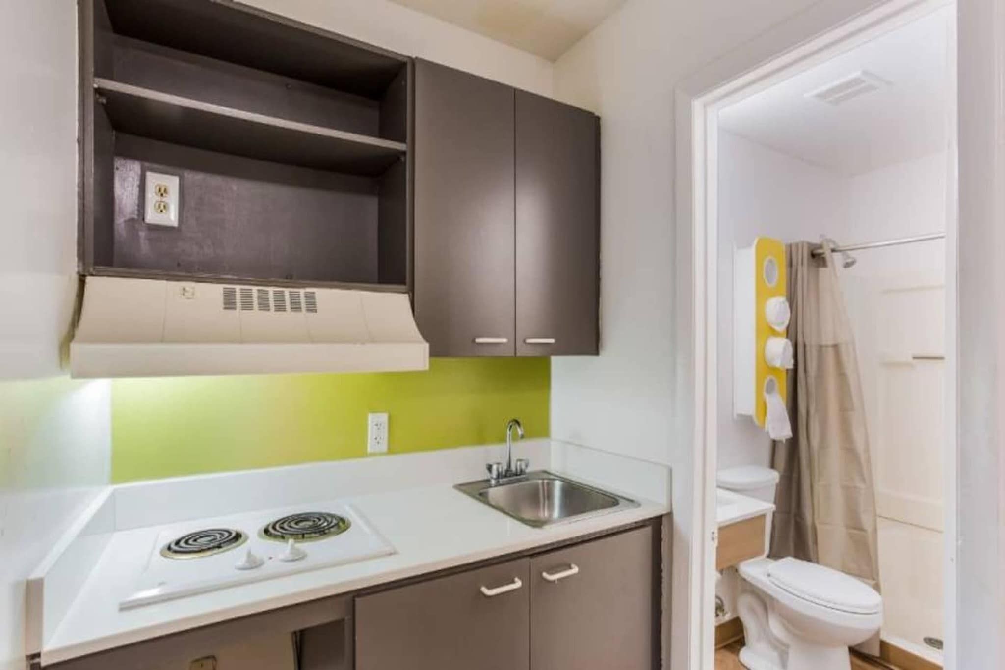 A compact kitchen with a gas stove, a sink, and a toilet visible in the adjacent bathroom.