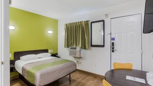 A hotel room with a bed, a bedside table, a chair, a desk, a mirror, an air conditioning unit, and a door. - 2Full Bed Non-Smoking|Jacksonville (Jacksonville)