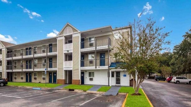 A multi-story hotel with a central courtyard, parking lot, and a small tree. - 2Full Bed Non-Smoking|Jacksonville (Jacksonville)