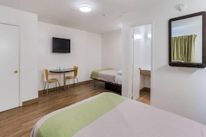 Habitación de hotel con cama, escritorio con dos sillas, televisor en la pared y espejo.