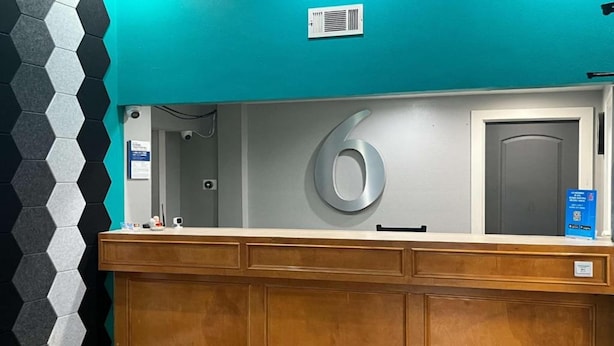 A reception desk with a large number '6' sign, a security camera, and a blue informational sign. - 2 Queen Beds|Smoking,Micfridge (Morrilton)