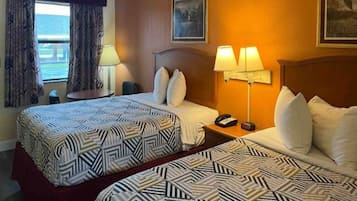 Une chambre d’hôtel avec deux lits, une table de chevet avec une lampe, un téléphone et une fenêtre avec des rideaux.