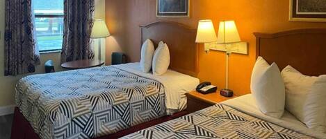 A hotel room with two beds, a nightstand with a lamp, a telephone, and a window with curtains.