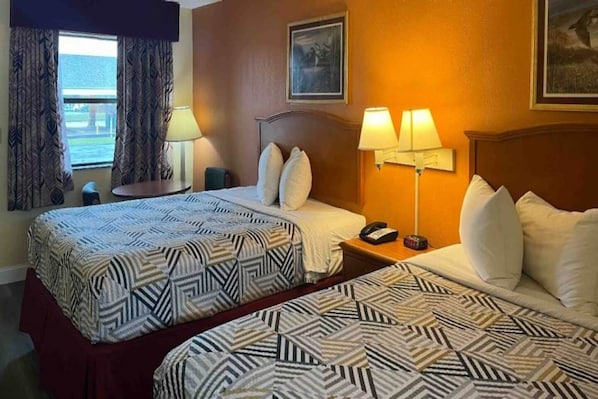 A hotel room with two beds, a nightstand with a lamp, a telephone, and a window with curtains.