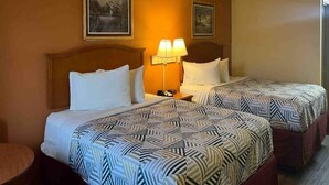 A hotel room with two beds, each with patterned bedding, a nightstand with a lamp, and framed artwork on the walls. - 2 Queen Beds|Smoking,Micfridge (Morrilton)