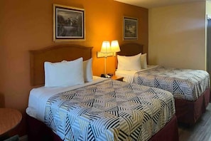 Quarto de hotel com duas camas, cada uma com roupa de cama estampada, uma mesa de cabeceira com abajur e quadros nas paredes.