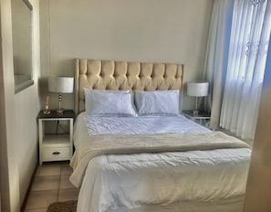 Ein Hotelzimmer mit einem großen Bett, zwei Nachttischen, einem Spiegel und einem Fenster mit Vorhängen.