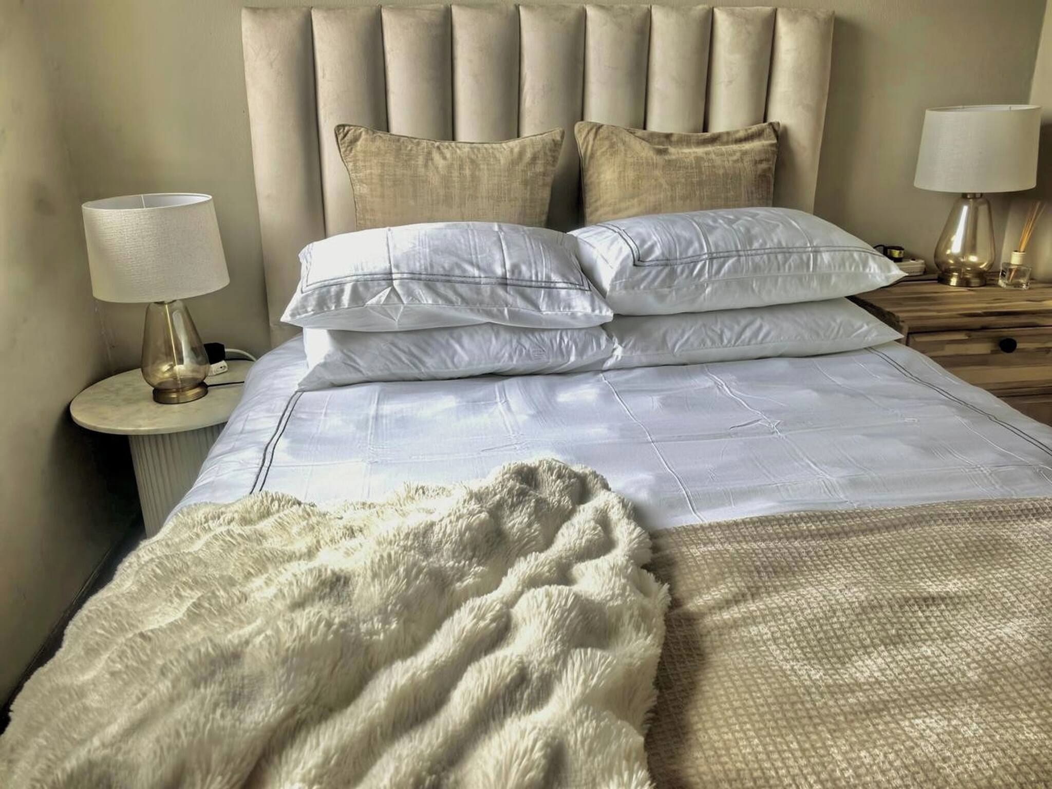 A neatly made bed with a fluffy white throw blanket, a headboard with vertical panels, and two bedside lamps on wooden nightstands.
