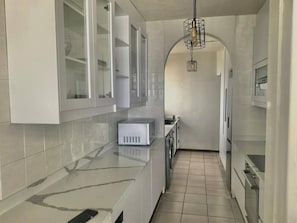 A modern kitchen with white cabinets, a marble countertop, and a built-in oven. - 10 C-Front Penthouse (Margate)