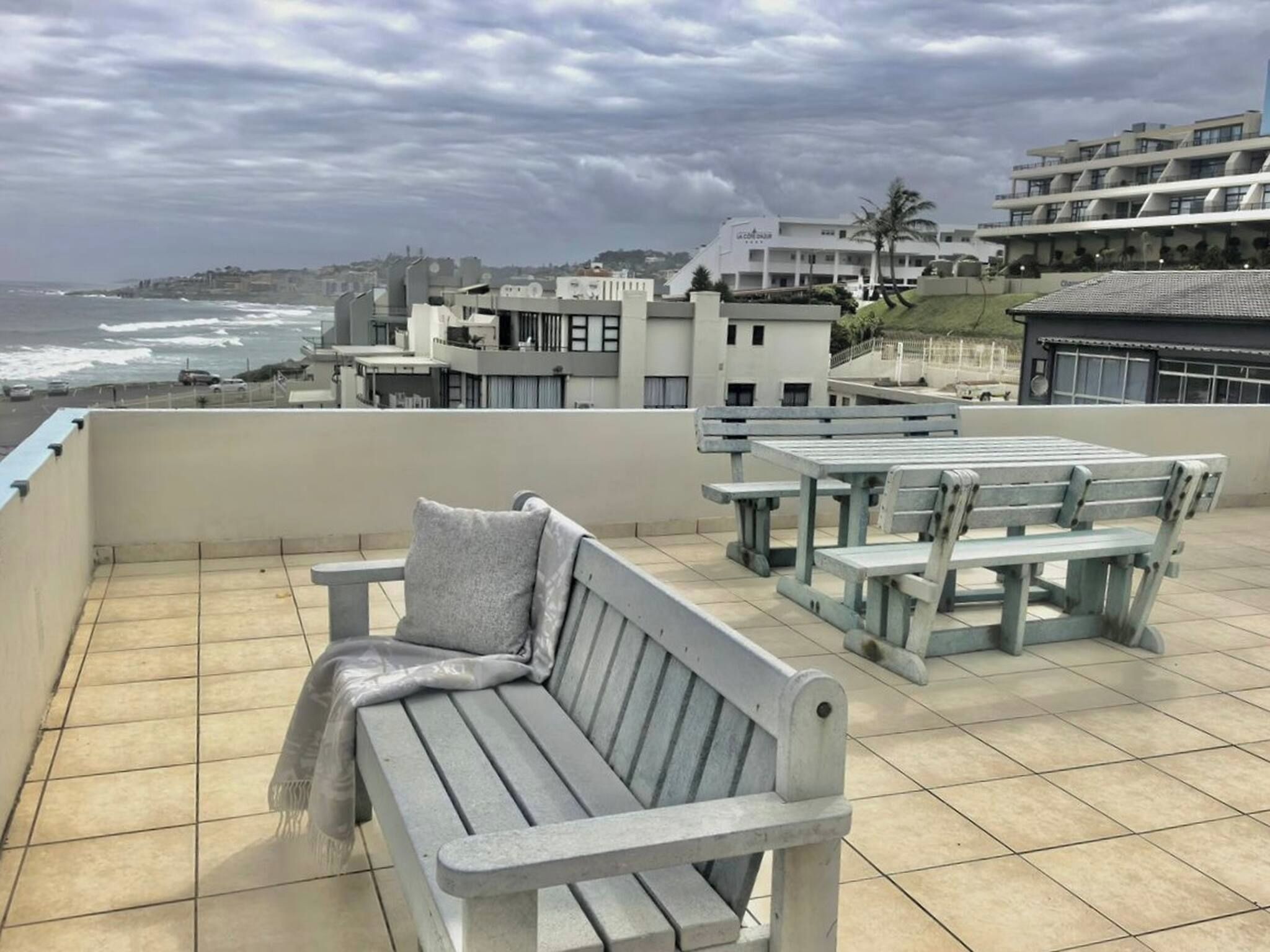 Een terras met een bankje en tafels, met uitzicht op een kustgebied met gebouwen en de zee.
