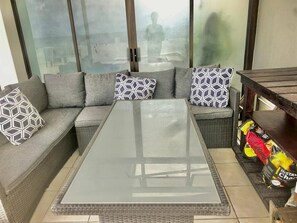 A modern living room with a glass-top coffee table, grey sofa with patterned cushions, and a wicker side table with a bag of chips. - 10 C-Front Penthouse (Margate)