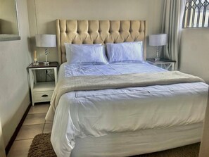 Habitació d'hotel amb un llit gran, dues taules de nit i una finestra amb reixes.