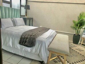 A bedroom with a bed, bedside tables, a lamp, a plant, and a window. - 10 C-Front Penthouse (Margate)