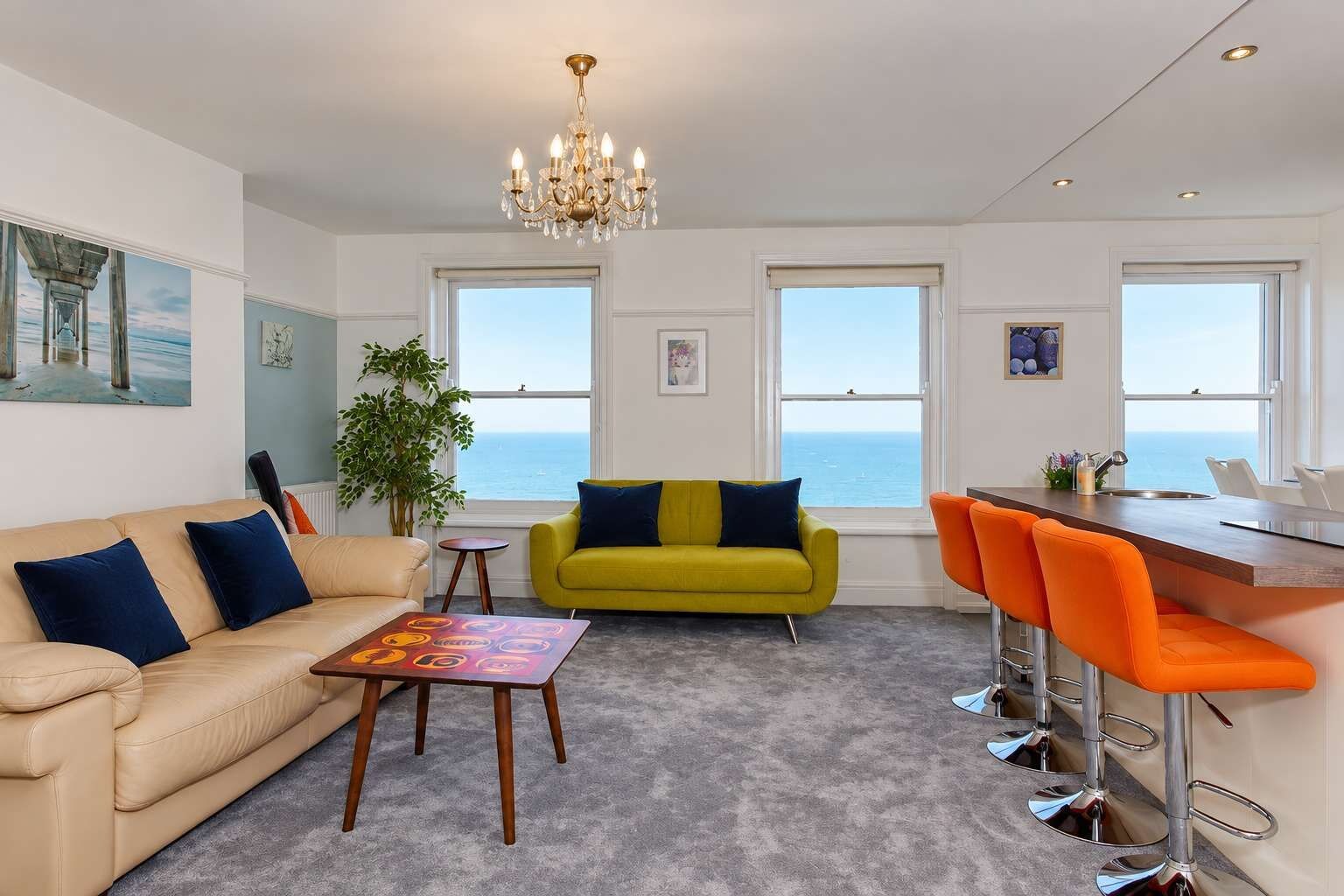 A modern living room with a sofa, a yellow armchair, a coffee table, and a bar area with orange chairs.