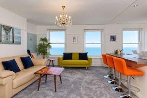 A modern living room with a sofa, a yellow armchair, a coffee table, and a bar area with orange chairs. - Horizon View | Quirky | Sea Views | Long stays (Ramsgate)
