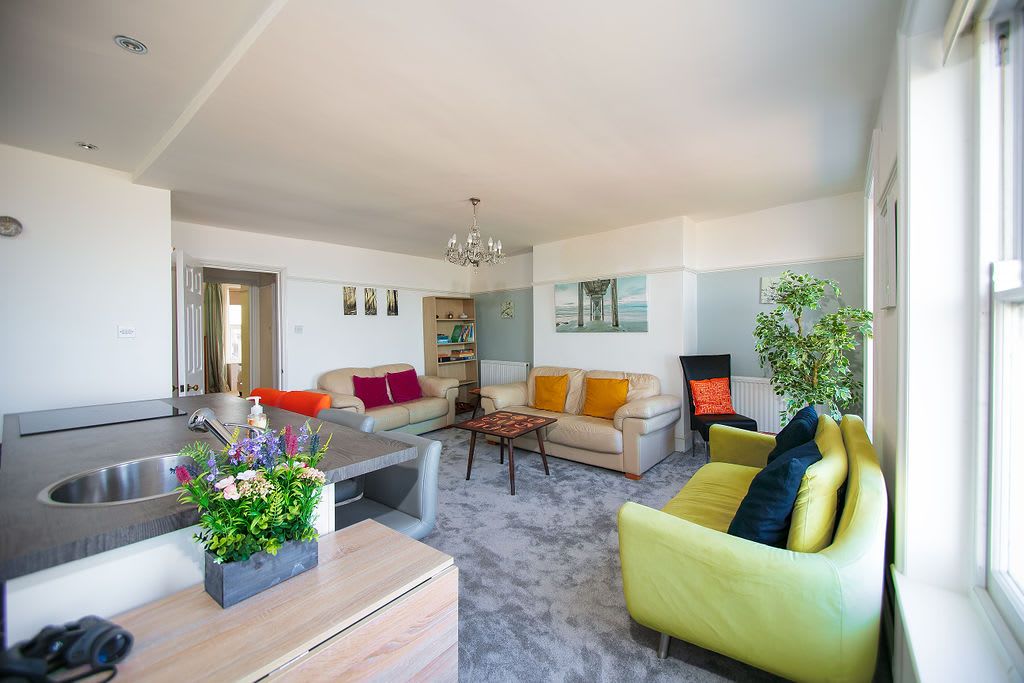 A modern living room with a sofa, coffee table, and a dining area with a sink and flowers.