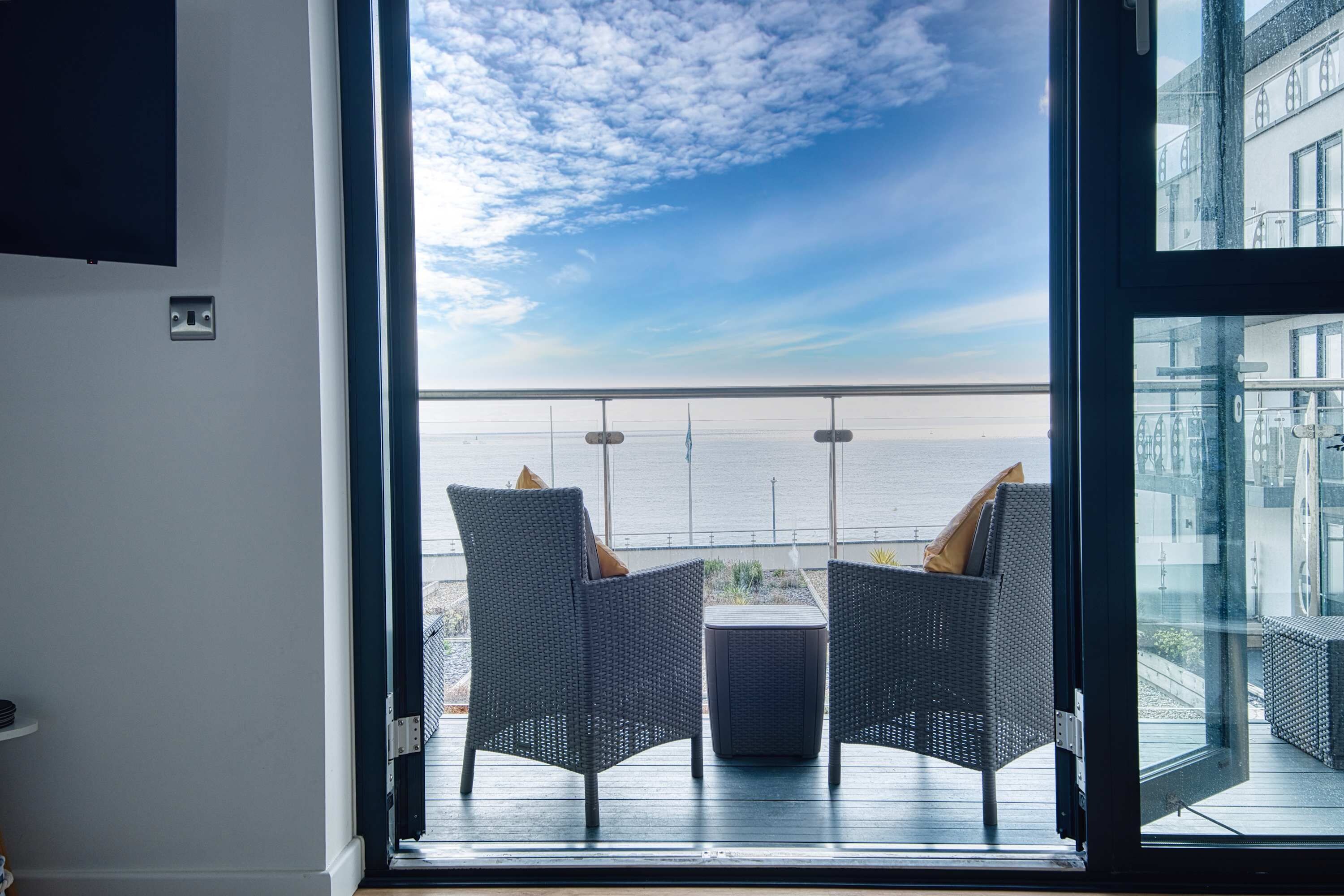 A room with a large window overlooking a balcony with two wicker chairs and a small table.