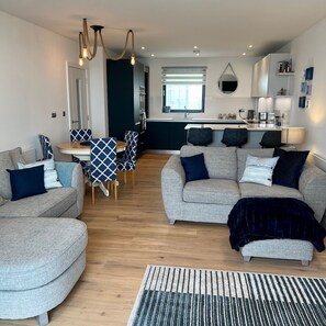 Ein modernes Wohnzimmer mit einer Sofagarnitur, einem Essbereich mit Tisch und Stühlen sowie einer Küche im Hintergrund.