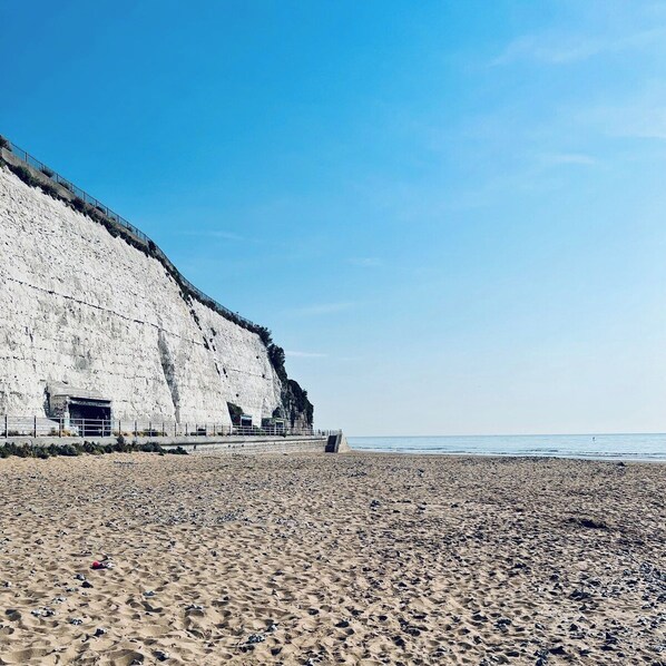 Ein Strand mit einer hohen, weißen Klippe und einem gepflasterten Weg.