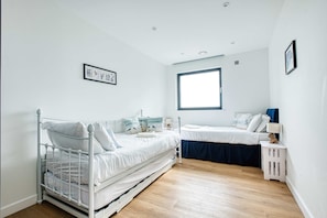 Ein Schlafzimmer mit einem Bett, einem Einzelbett, einem Fenster und einem an der Wand befestigten Regal.