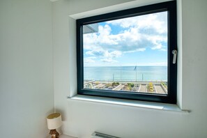 A room with a window overlooking a coastal view, a radiator, and a small lamp. - Seafront Retreat |Beach Access |Sea Views, Parking (Ramsgate)
