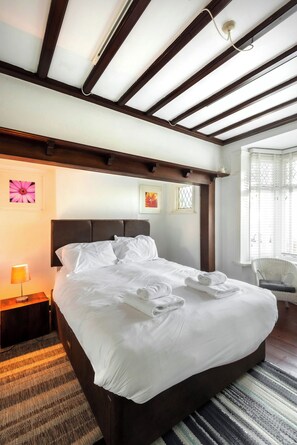 A hotel room with a large bed, a nightstand with a lamp, a chair, and artwork on the walls. - Montefiore | Charm | Quiet | Parking | Long Stays (Ramsgate)