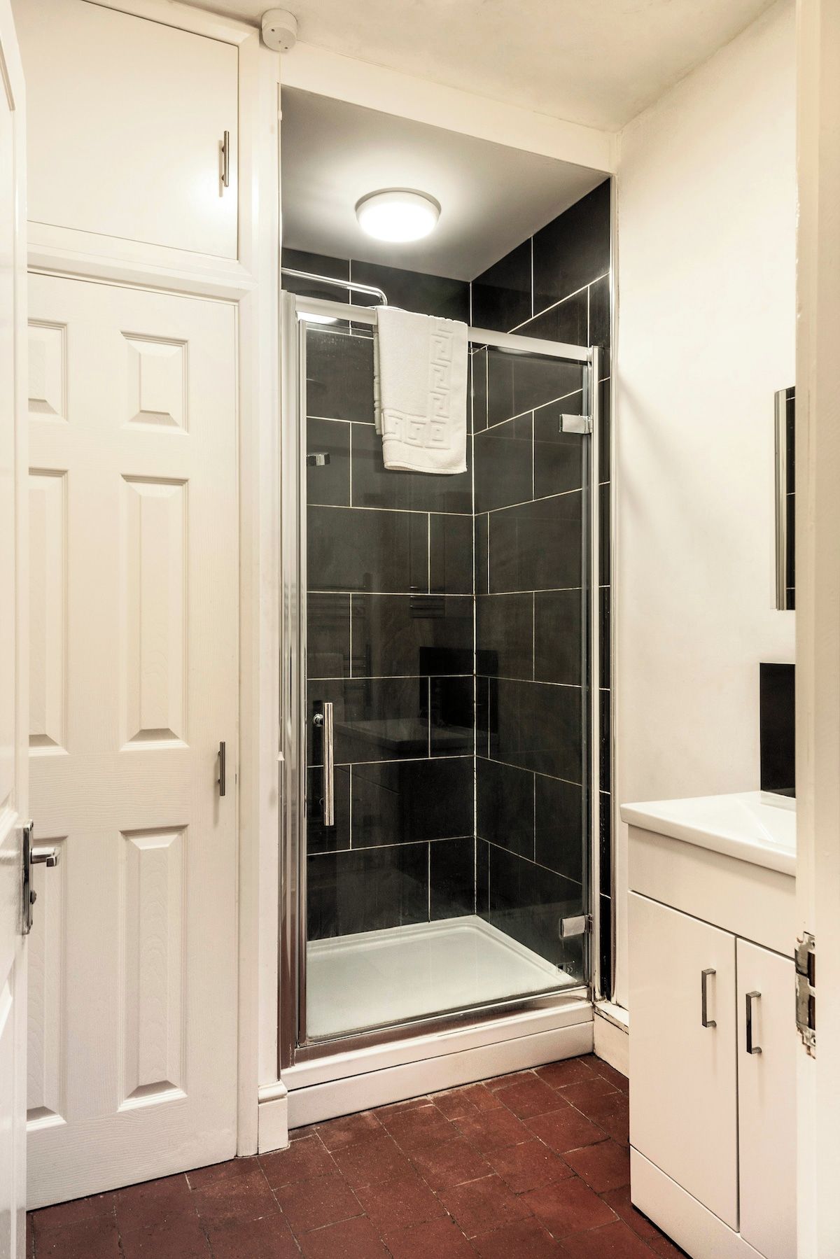 A bathroom with a glass-enclosed shower, white cabinetry, and a tiled floor.