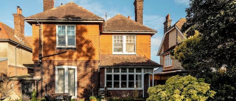 Una casa de dos pisos con un patio a cuadros, una chimenea y una ventana con contraventanas.