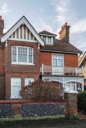 A two-story house with a brick facade, white window frames, and a small balcony with a white railing. - Montefiore | Charm | Quiet | Parking | Long Stays (Ramsgate)
