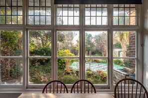 Een kamer met een groot raam met uitzicht op een tuin met diverse planten en een geruit gazon.