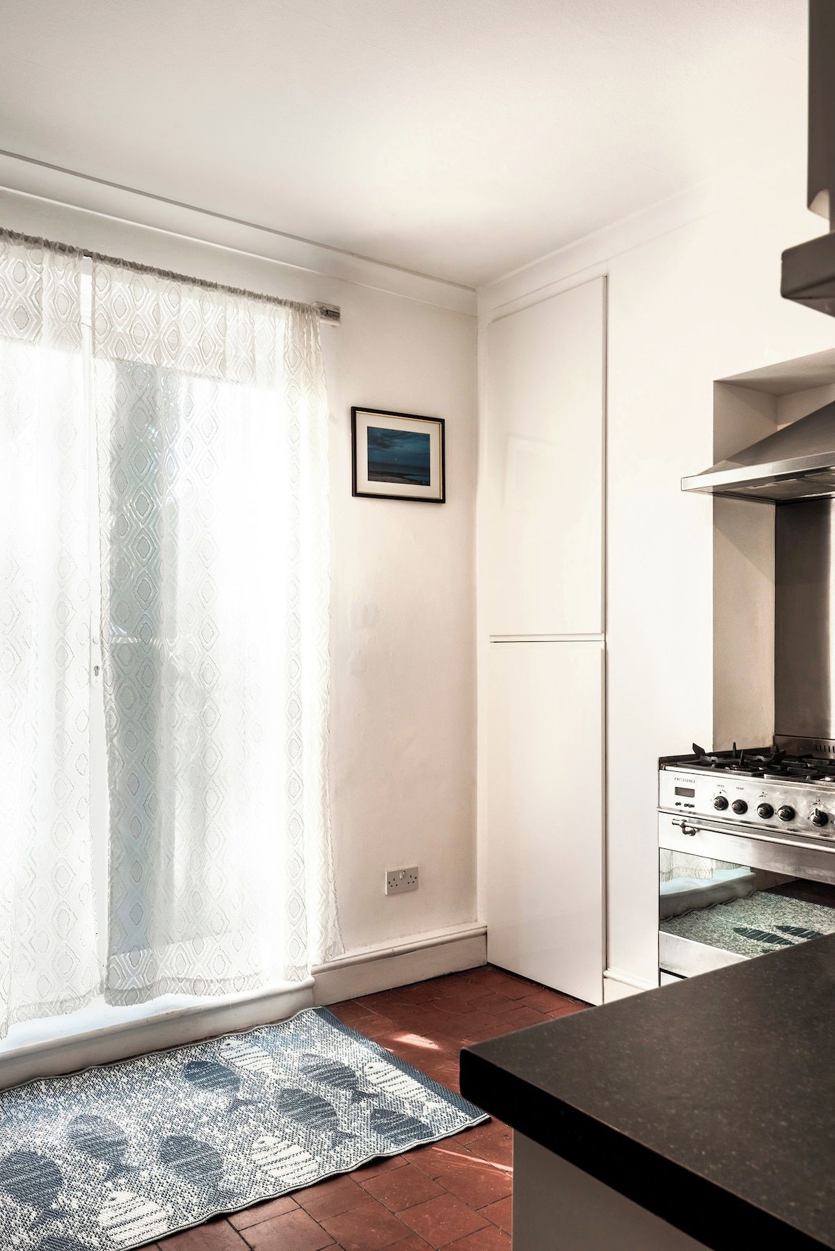 A compact kitchen with a gas stove, a refrigerator, and a patterned rug on the floor.