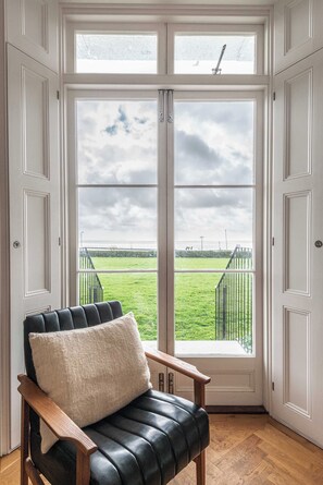 A room with a large window, a black leather chair with a white cushion, and a wooden floor. - Royal Channel Retreat | Peaceful Sea Views (Ramsgate)