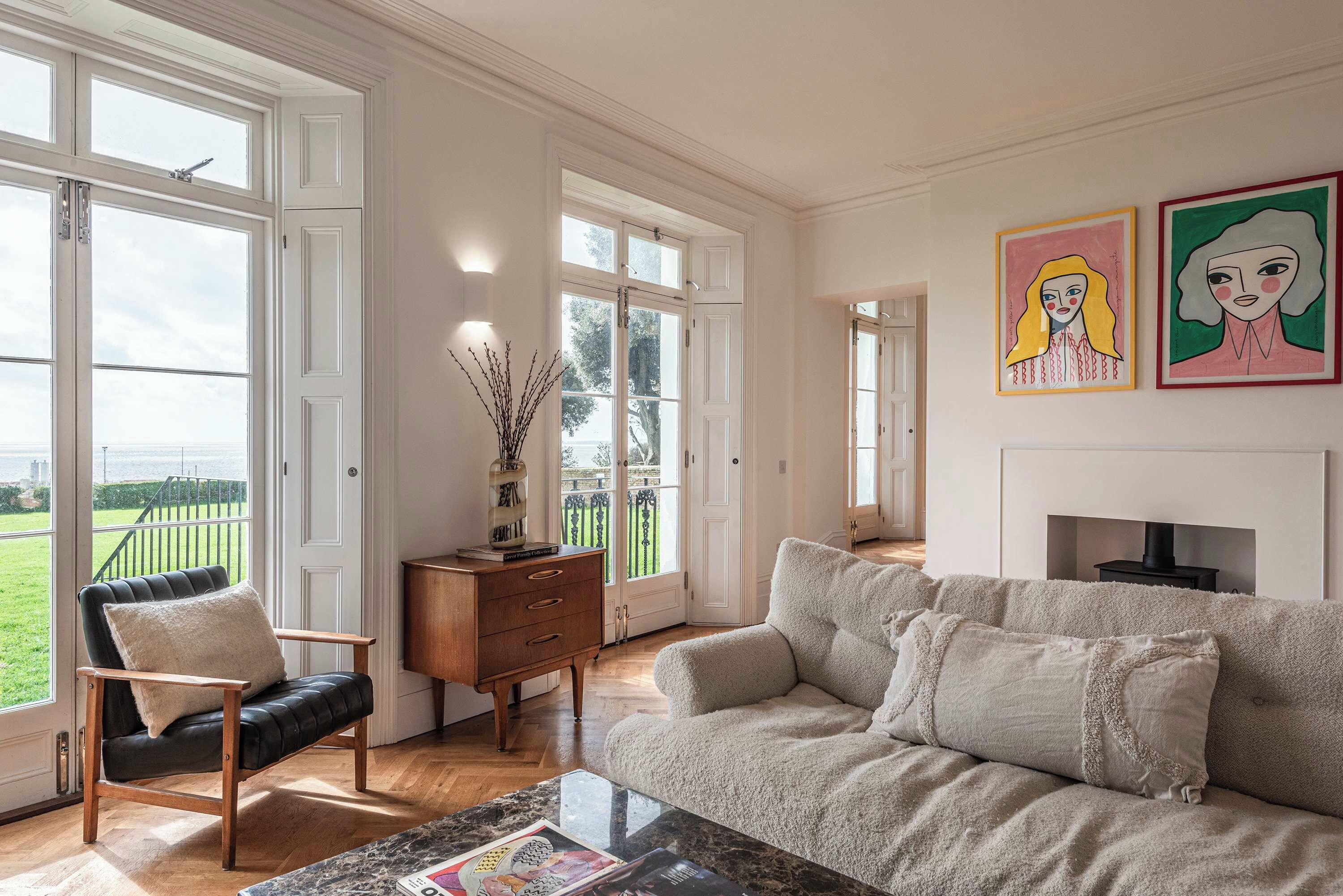 Un salón espacioso con un gran ventanal, una chimenea y dos cuadros en la pared.