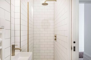 A bathroom with white tiled walls, a shower with a gold showerhead, and a sink with a gold faucet. - Royal Channel Retreat | Peaceful Sea Views (Ramsgate)