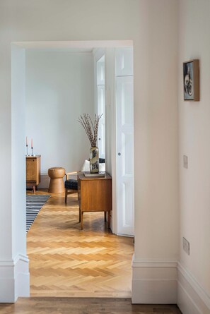 A hallway with a wooden herringbone floor, a white door, a wooden bench, a small round stool, and a vase with branches. - Royal Channel Retreat | Peaceful Sea Views (Ramsgate)